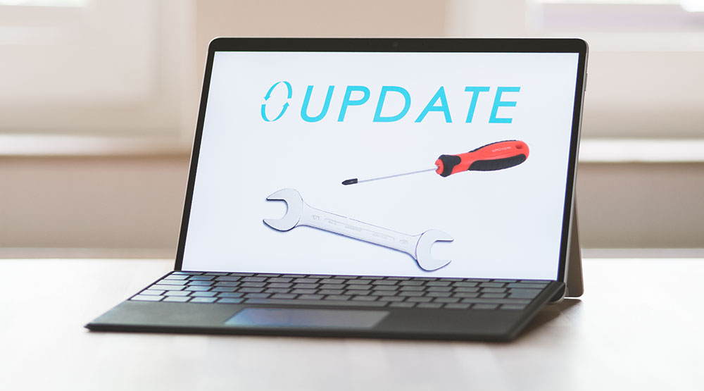 Auf einem hellen Tisch stehendes Laptop mit aufgeklapptem Bildschirm, auf dem das Wort 'UPDATE' sowie das Symbol eines Schraubenschlüssels und eines Schraubenziehers abgebildet sind